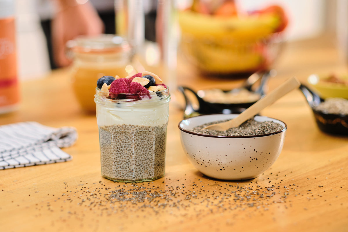 Chia pudding in a glass jar with yogurt and berries, next to a bowl of chia seeds