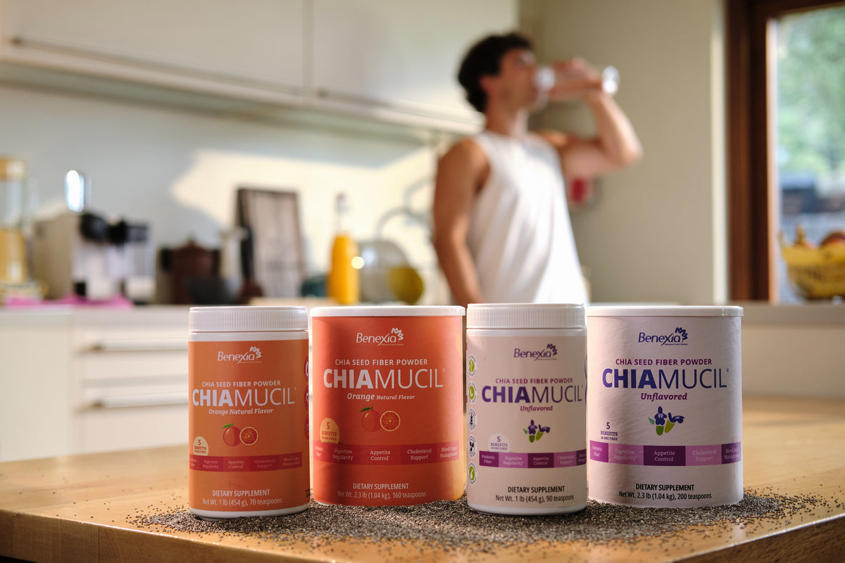 A man drinks from a glass behind ChiaMucil Orange and Unflavored tins, 1 lb and 2.3 lb