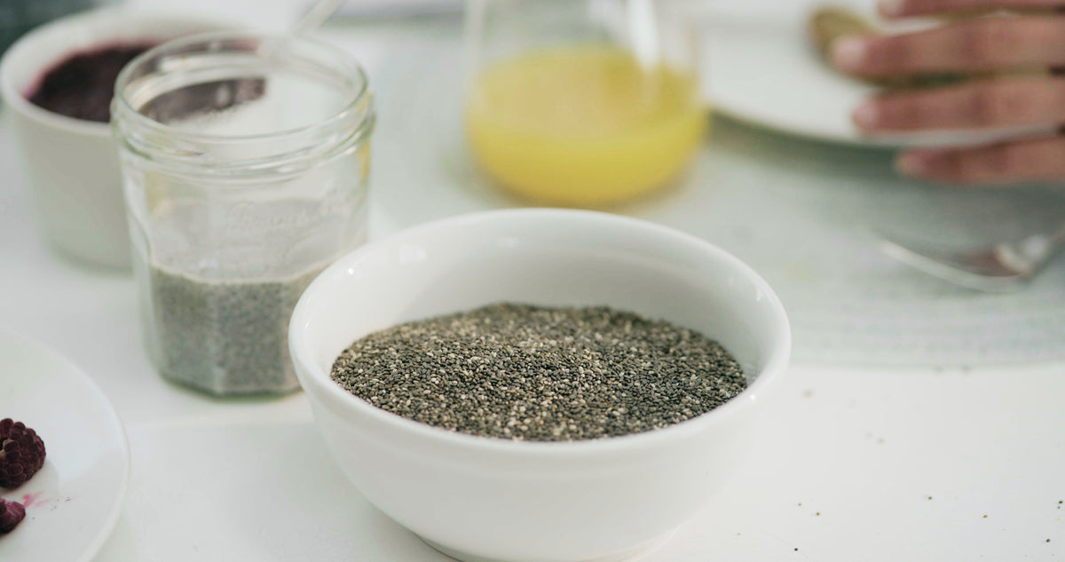 A bowl of chia seeds on a breakfast table, with a jar of soaked chia, orange juice and berries