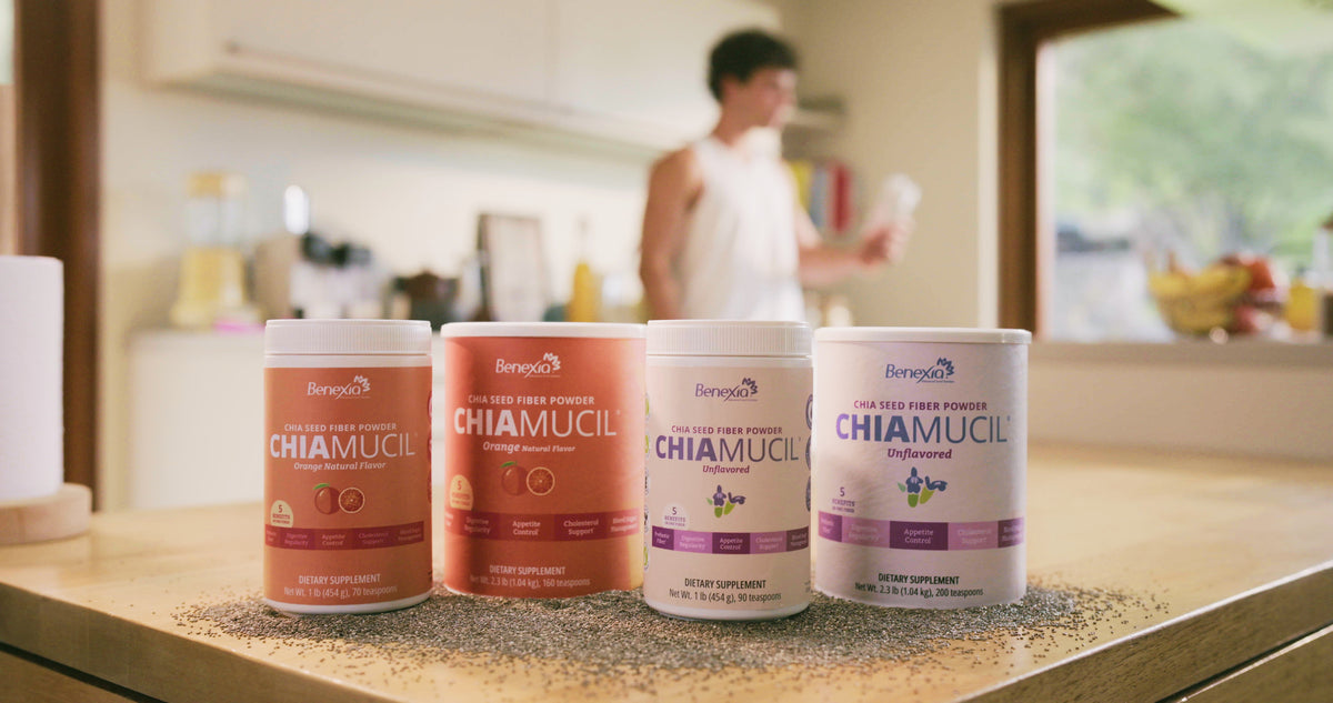 Four ChiaMucil tins on a kitchen counter scattered with chia seeds, someone drinking in the background